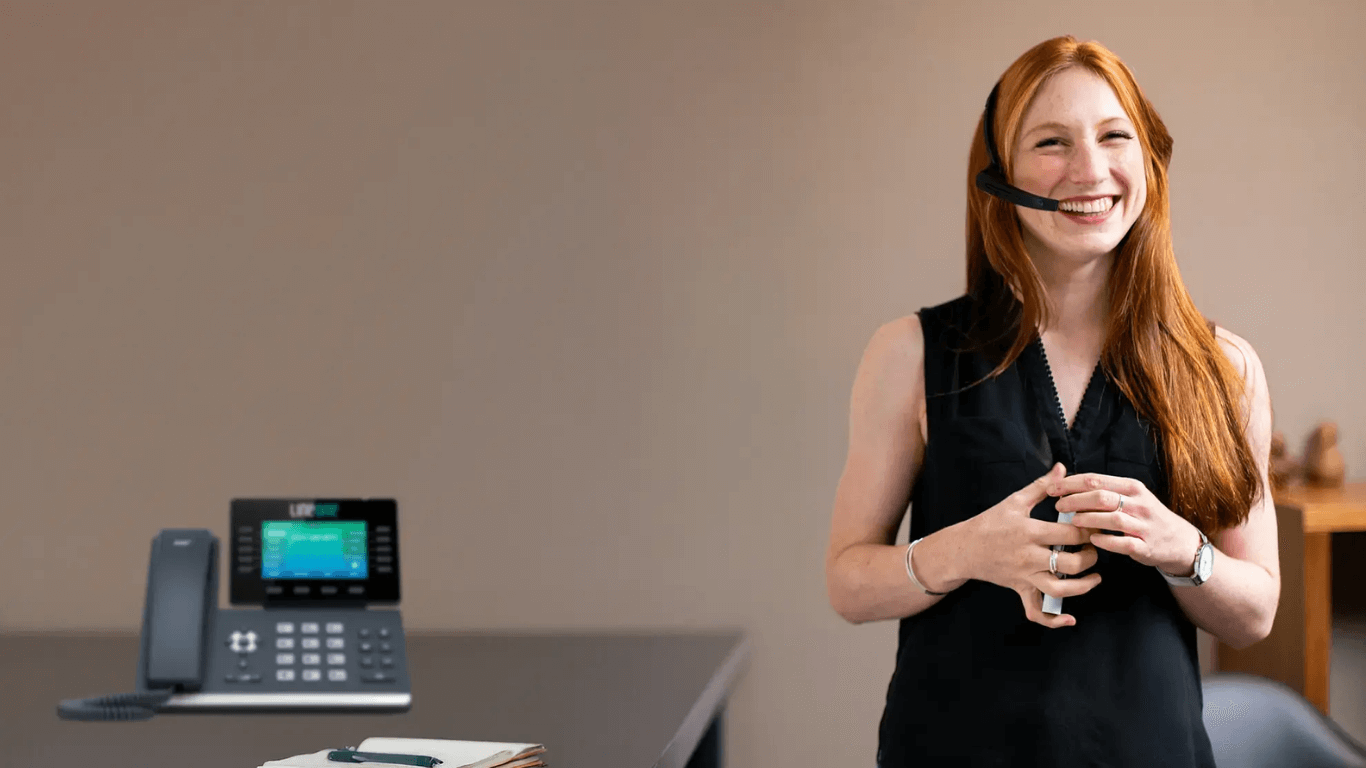 Customer support professional using a VoIP headset and desk phone, demonstrating modern business phone system productivity