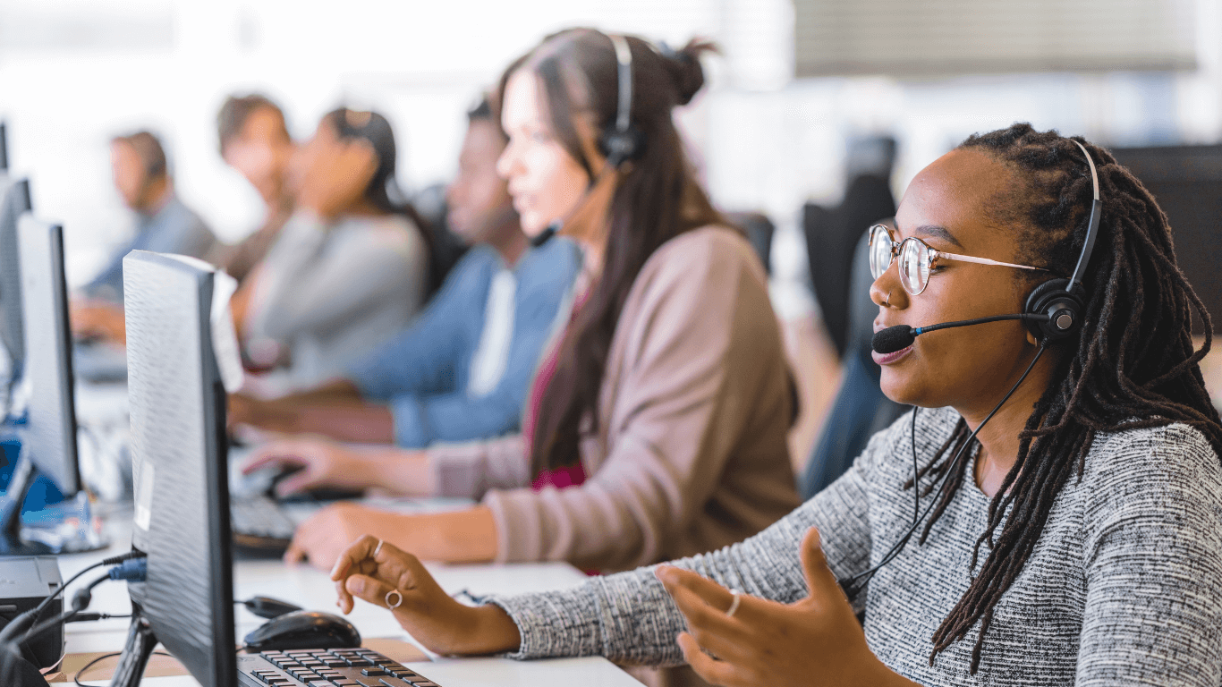 Call center agents using headsets and computers to manage customer calls efficiently with a cloud-based phone and call queue system.